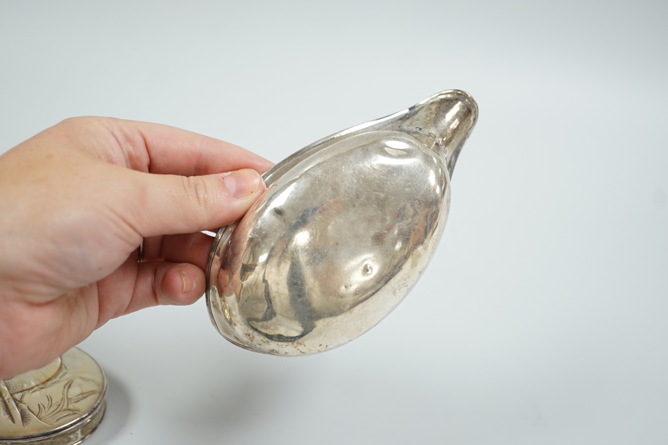 A late George III silver pap boat, London, 1817, 12.8cm, together with a 19th century white metal oval snuff, with inset mother of pearl cover, carved with fish, 8cm.